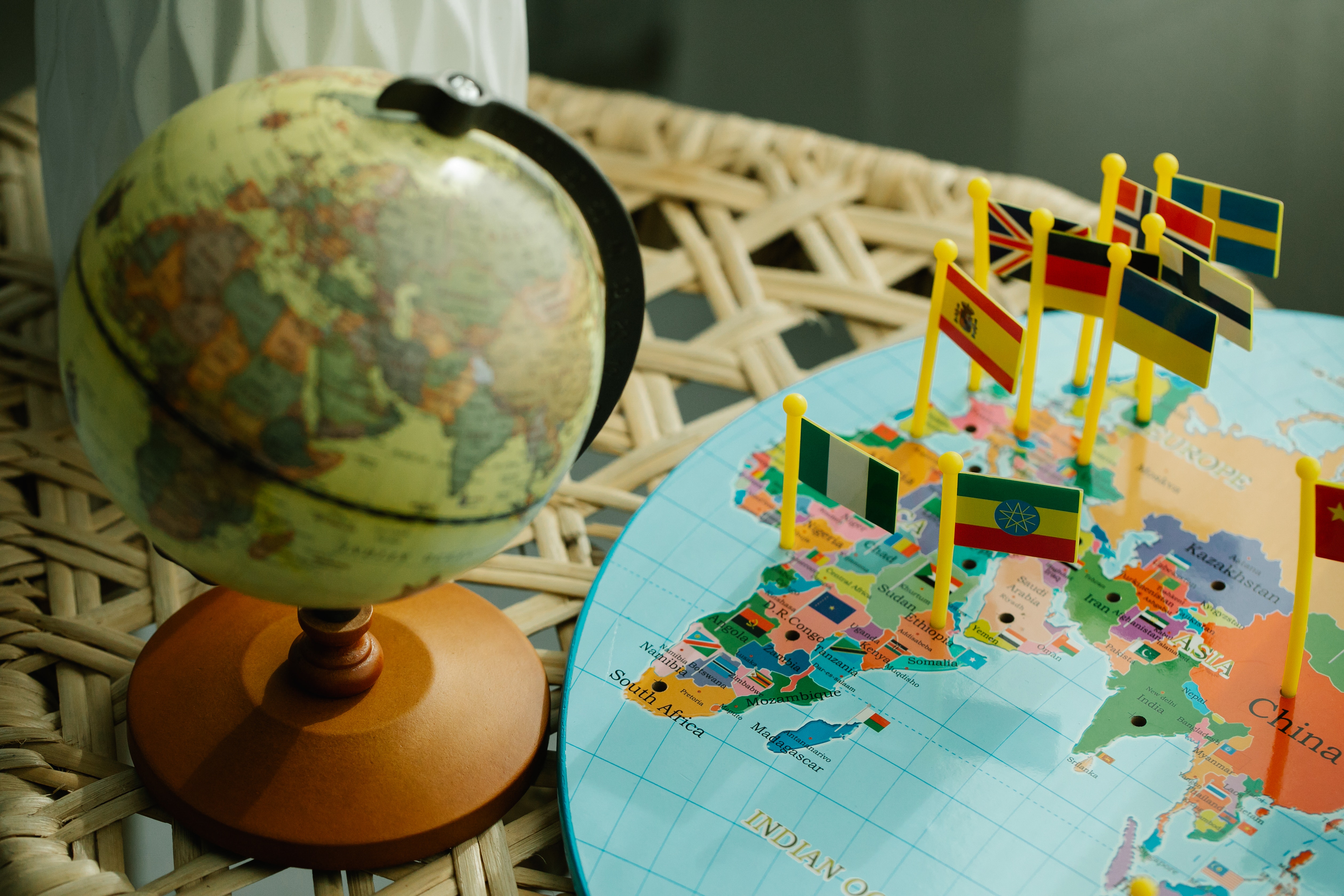 Photo by Lara Jameson retrieved from Pexels (https://www.pexels.com/photo/globe-and-a-flat-world-map-with-country-flag-markers-8828607/)